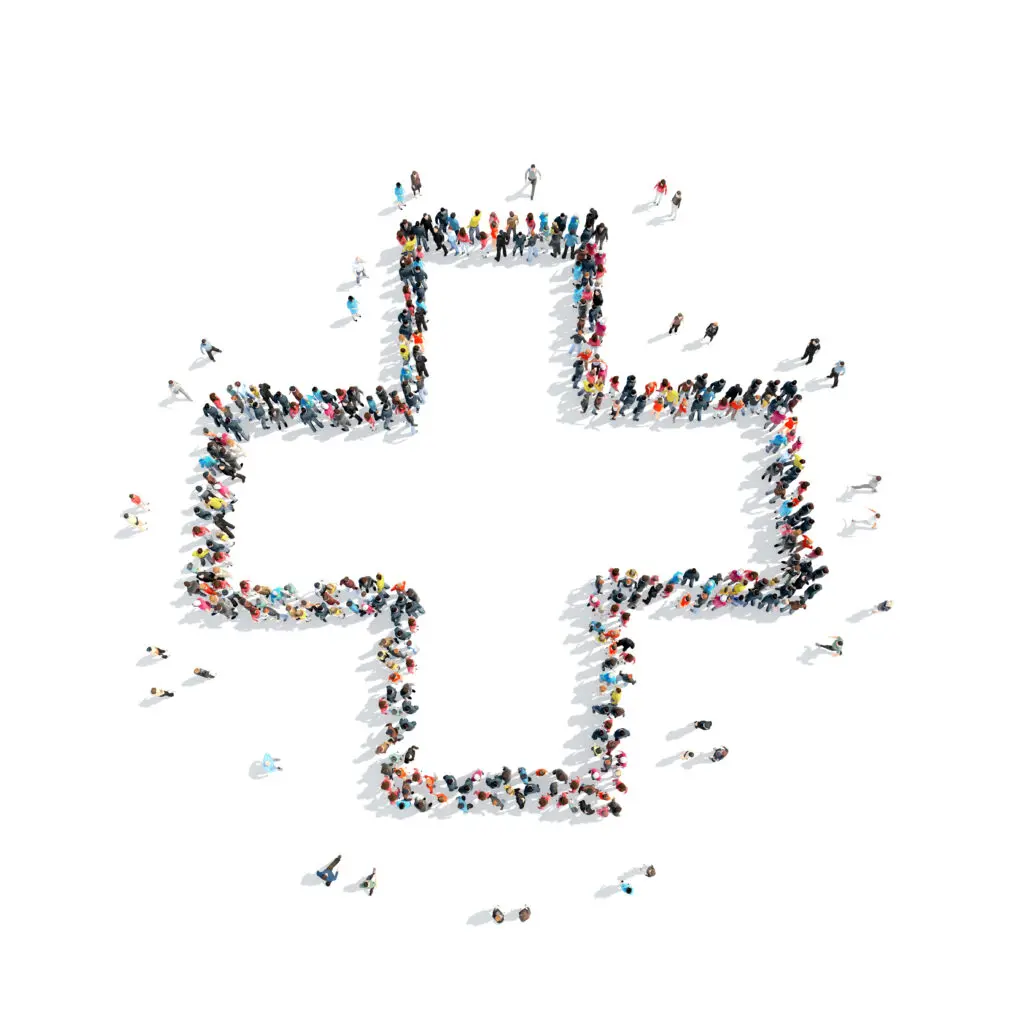 Large group of people stood up together to form the silhouette of a NHS cross, on a white background
