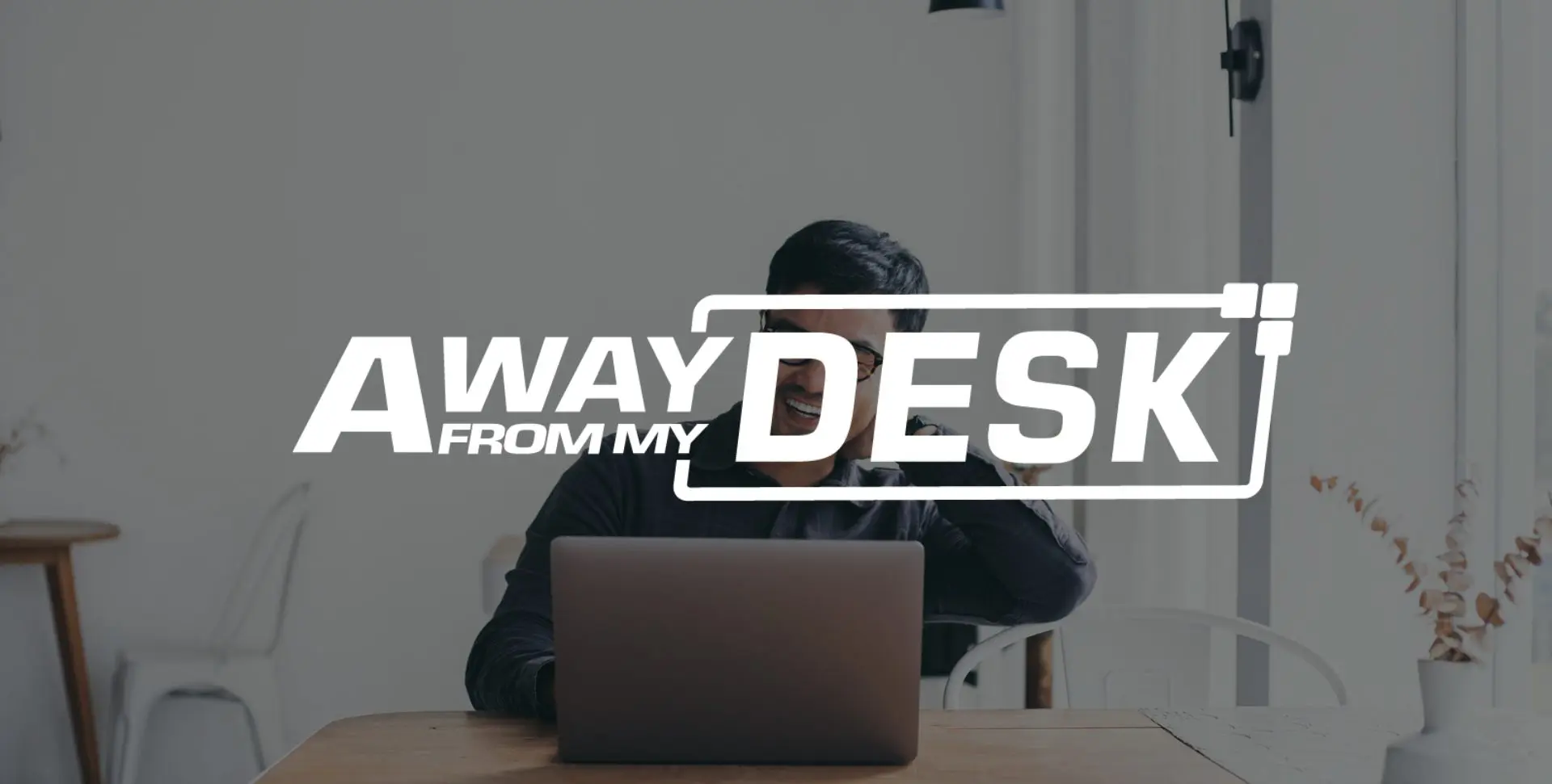 Man smiling on his laptop with the away from my desk logo on top of it