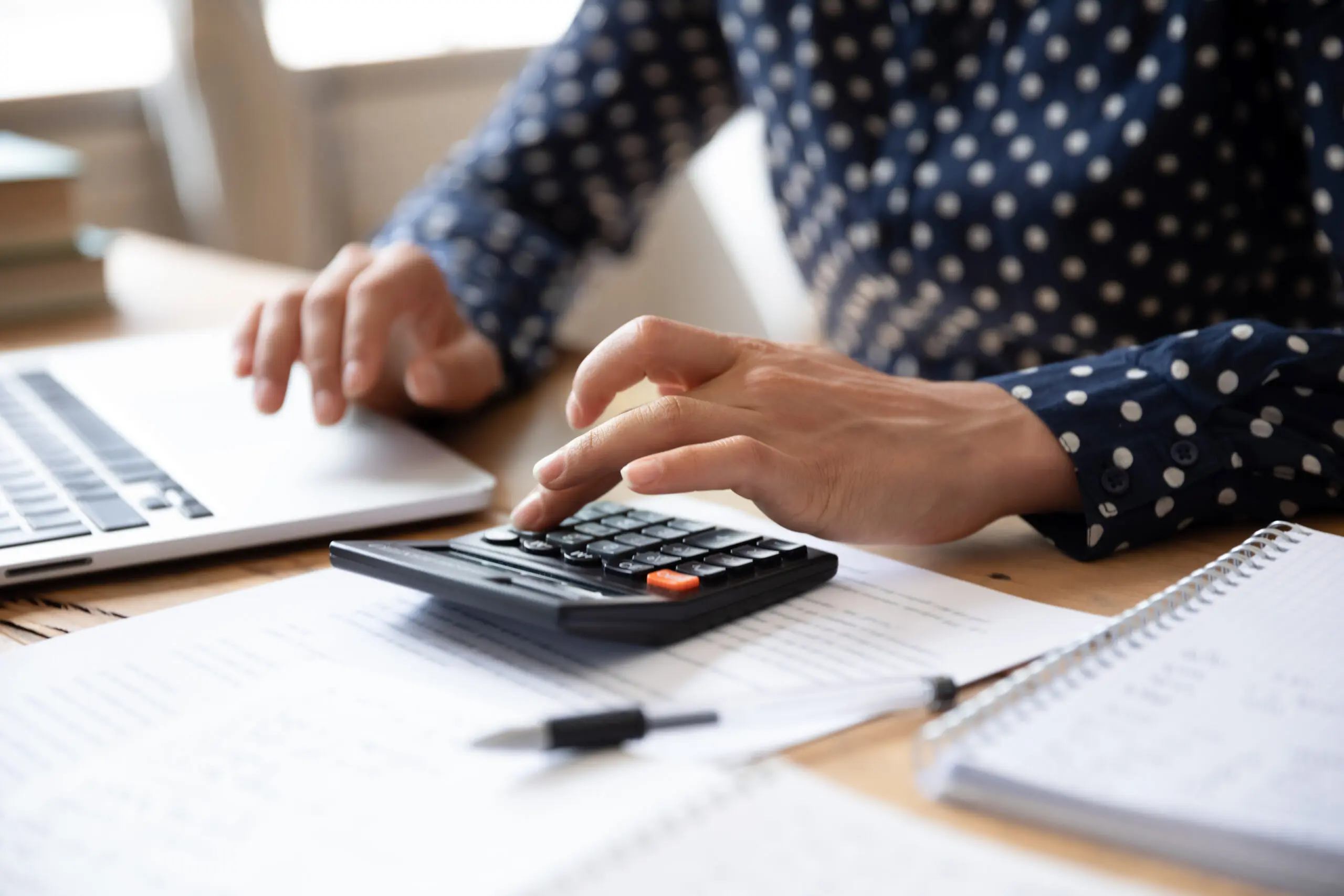 Close up woman using calculator and laptop with paperwork on her desk