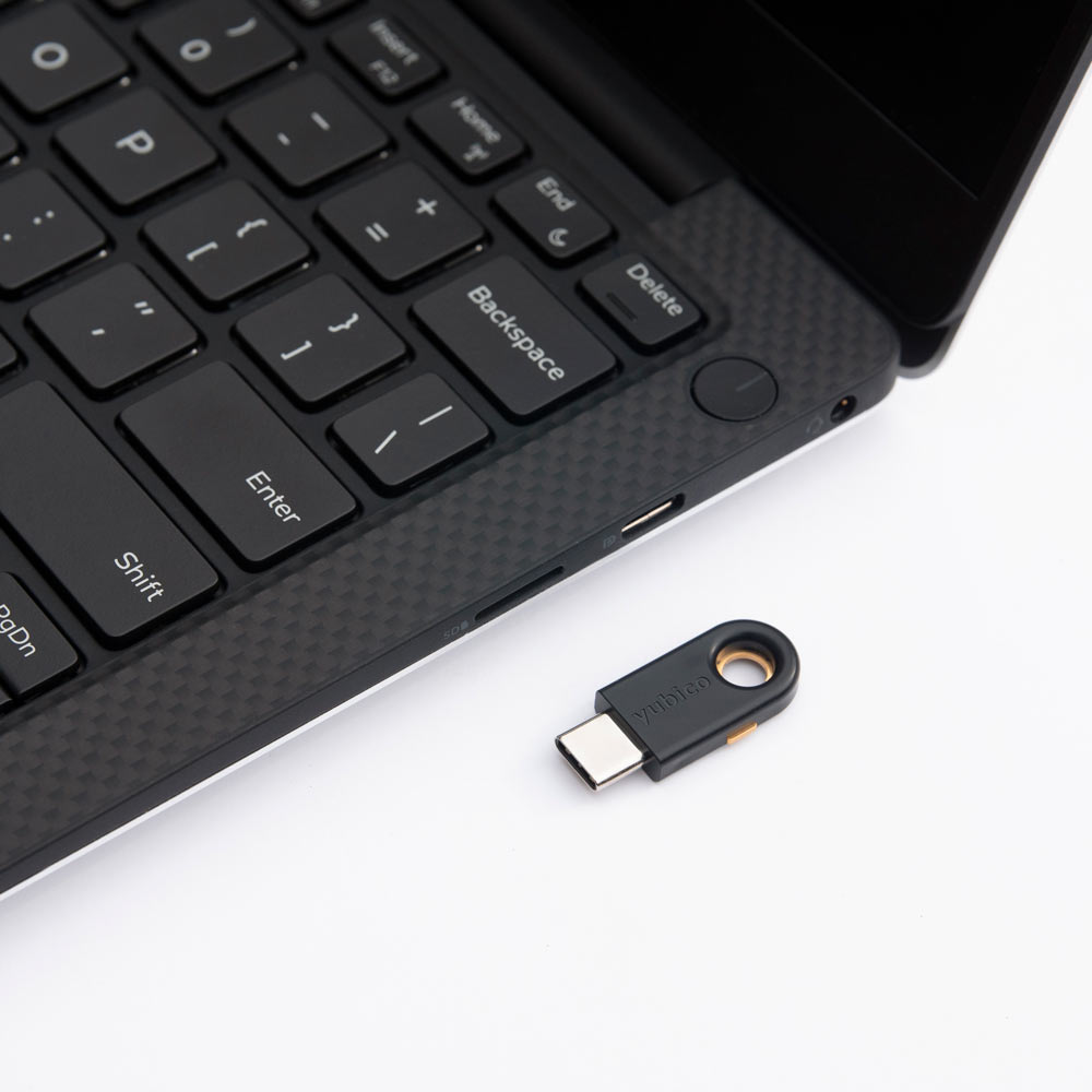 YubiKey 5c token laying flat on a surface next to a laptop