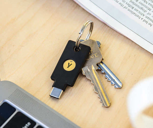 YubiKey 5c nfc on a keyring with two keys, placed down onto a wooden table next to a mac laptop