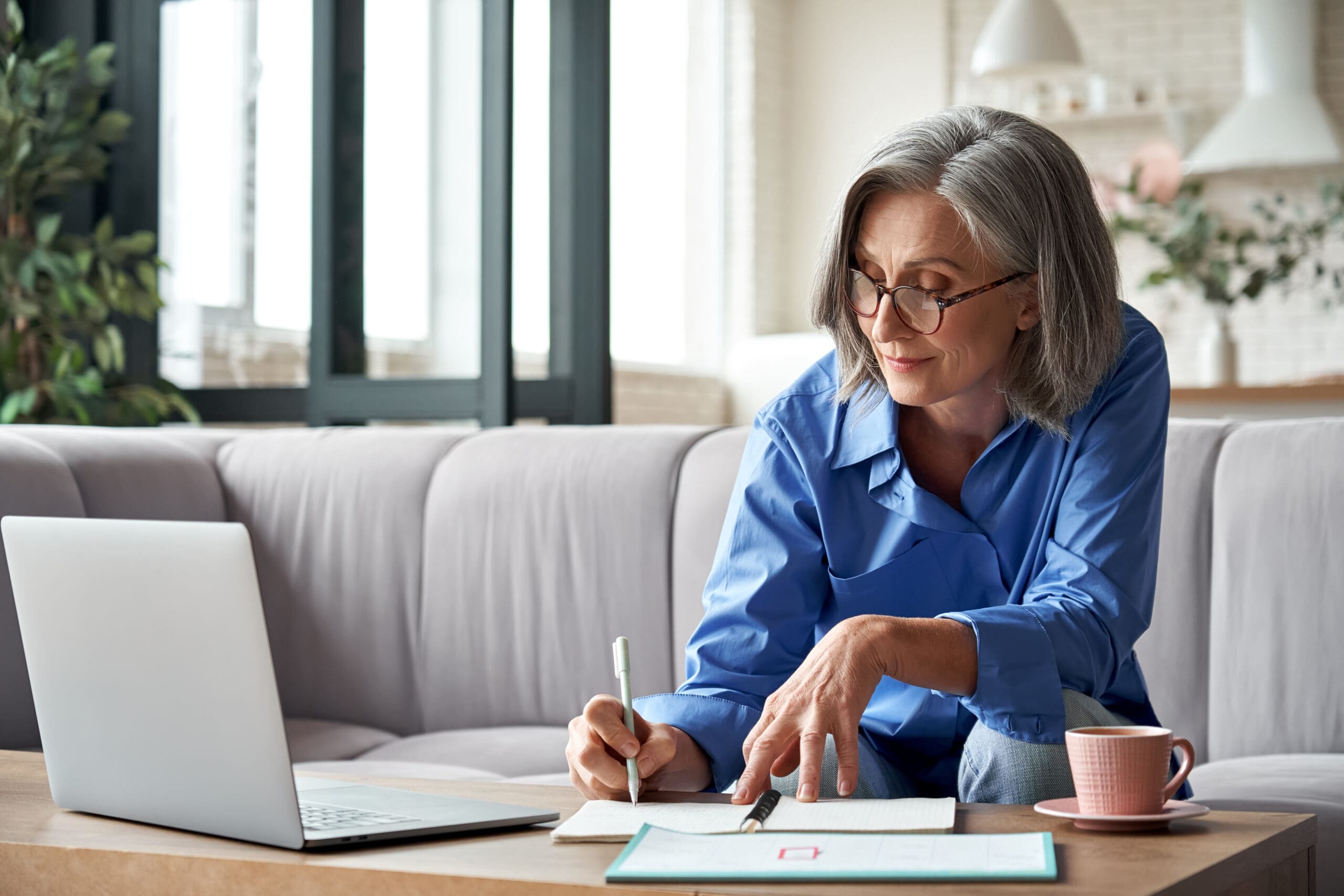 woman working from home on laptop taking notes in her notepad