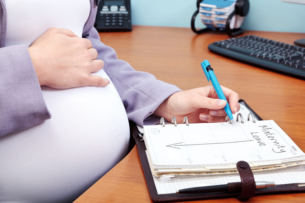 Pregnant lady sat at her desk filling in her maternity leave into her diary