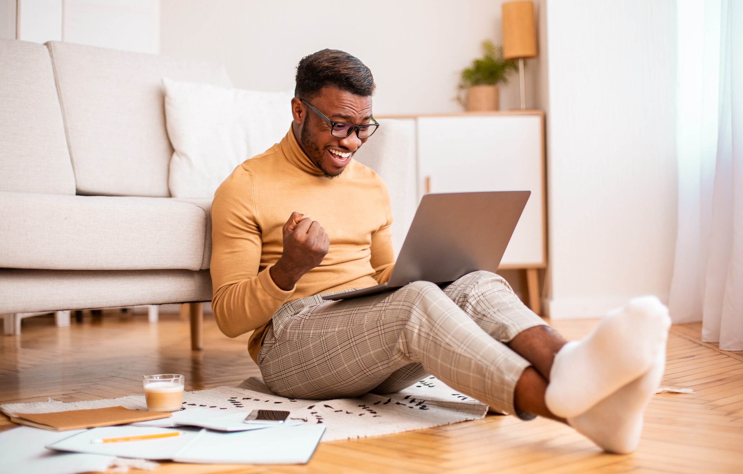 Excited guy using laptop shaking fists sitting at home on the floor with his laptop